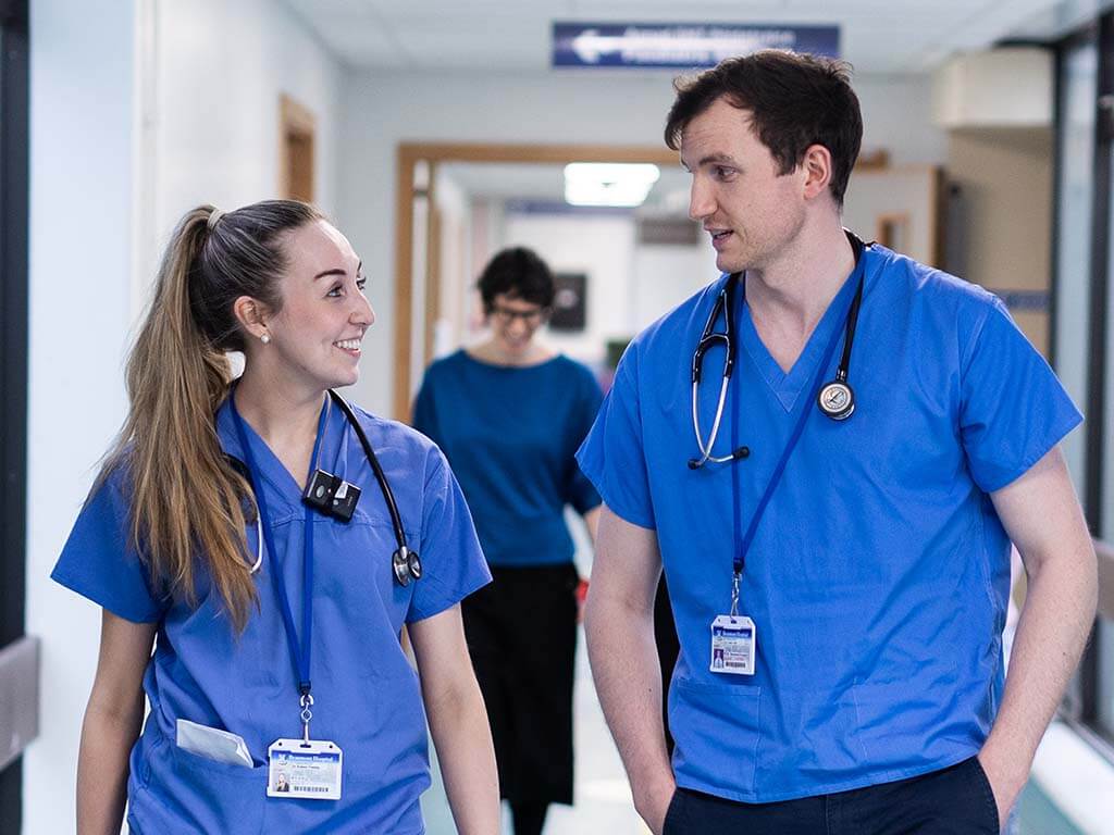2 Trainee doctors in scrubs walking in corridor